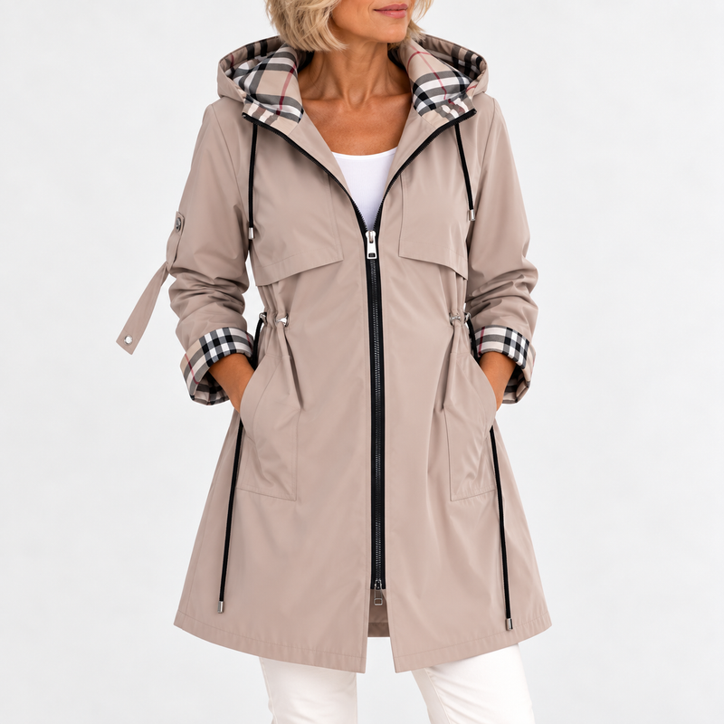 Voorkant van de jas in beige, gedragen met beide handen in de zakken, met trekkoord in de taille en geruite capuchonvoering. 2