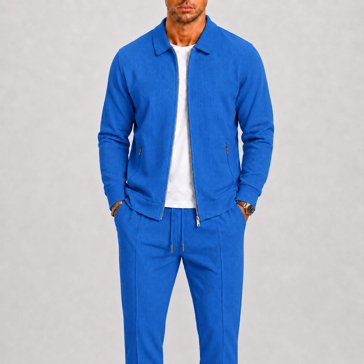Model draagt de set in felblauw met wafelstructuur, jack open over wit shirt, horloge om de pols 5