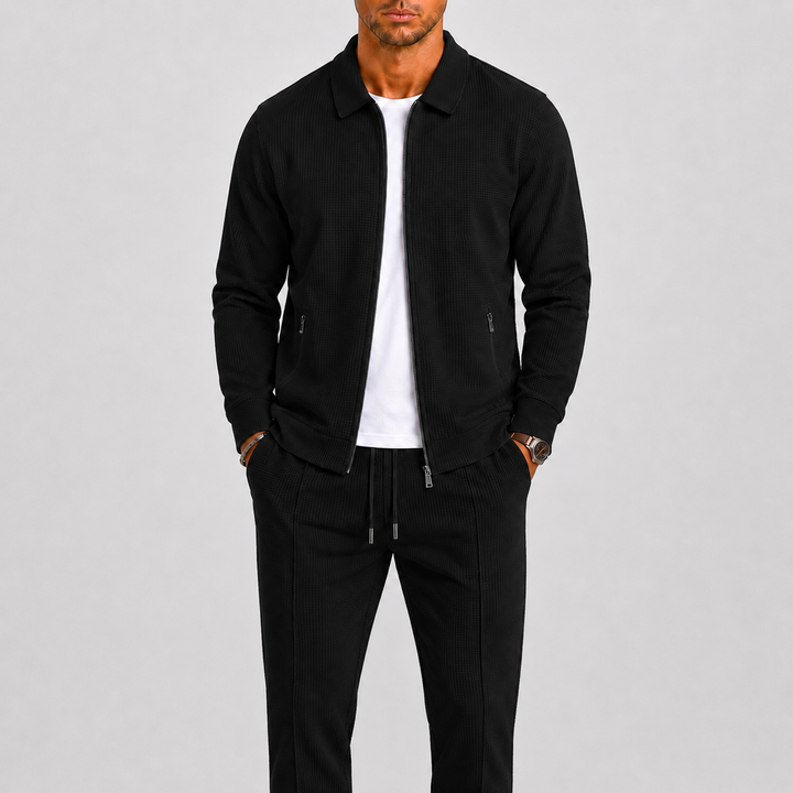 Model draagt de set in zwart met wafelstructuur, jack open over wit shirt, handen in zakken 3