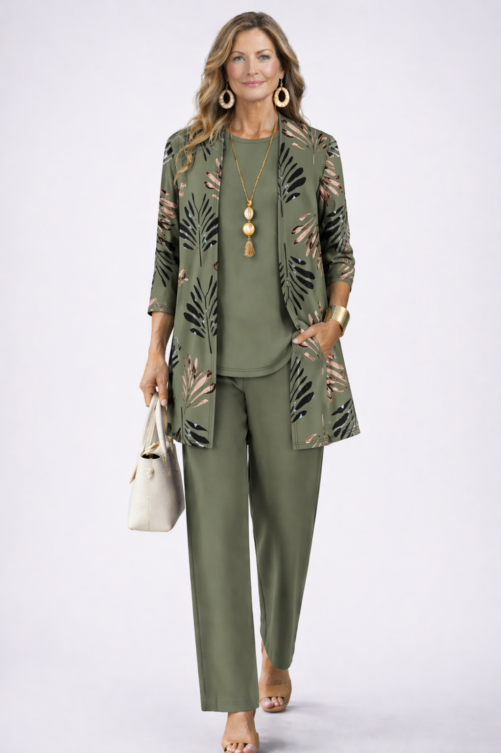 Model in olijfgroene set met vest met bladerprint, effen top, broek en witte handtas 1