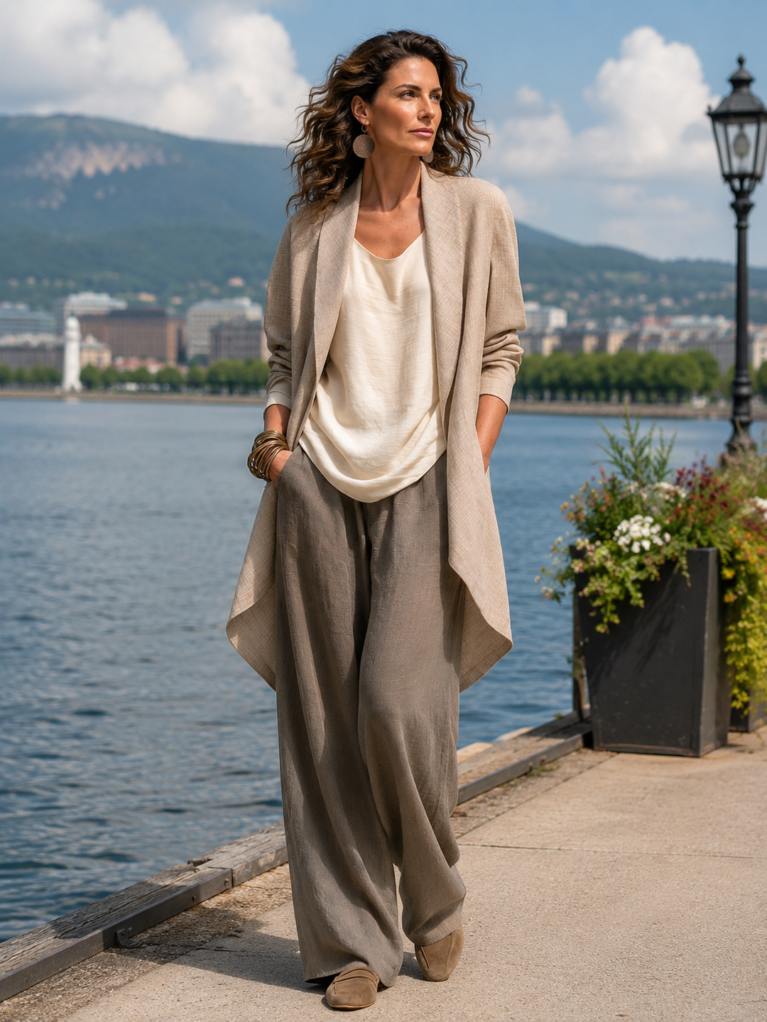 Model draagt de driedelige set buiten langs het water, met beige open jack, crèmekleurige top en taupe wijde broek. 7