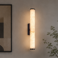 Brandende cilindervormige wandlamp van gemarmerd gesteente met donkere randen, naast een ingelijst abstract schilderij en een plant. 3