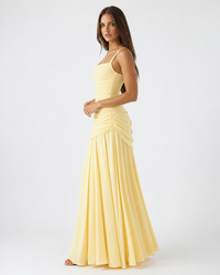 Lichtgele maxijurk in zijaanzicht op het model, met dunne bandjes, ruches langs de heup en een wijde chiffon rok. 3