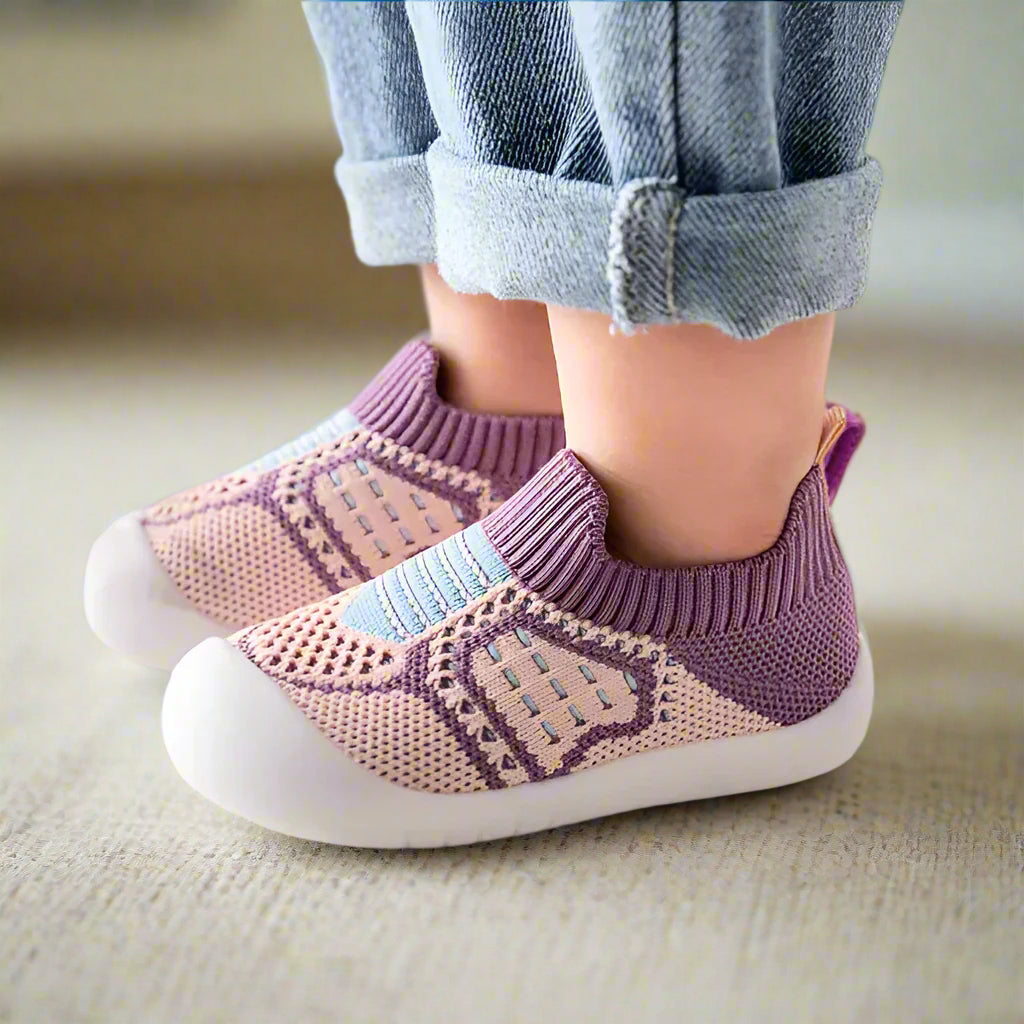 Paarse en roze gebreide babyschoentjes met geribbelde boord en blauwe streepjes, gedragen op een zachte beige ondergrond. 15