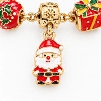 Close-up van een gouden kerstmanbedel in rode en witte emaille, tussen een hulstbedel en een rood cadeaubedel aan een armband. 3
