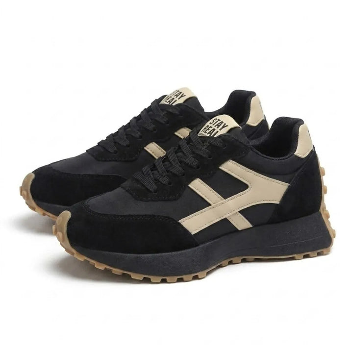 Paar zwarte sneakers met beige strepen en veters, schuin vooraanzicht op witte achtergrond 18