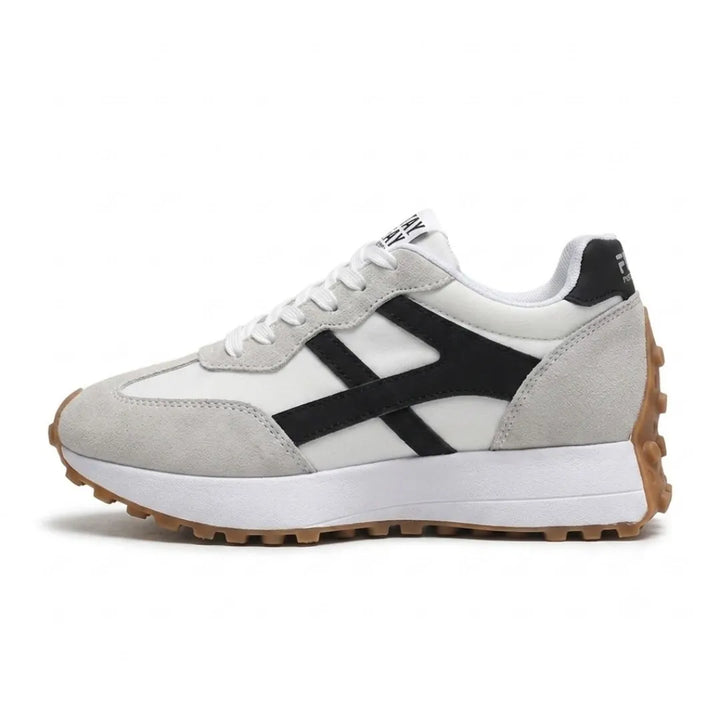 Zijaanzicht van een witte sneaker met grijze suède delen, zwarte accenten en bruine noppenzool 21