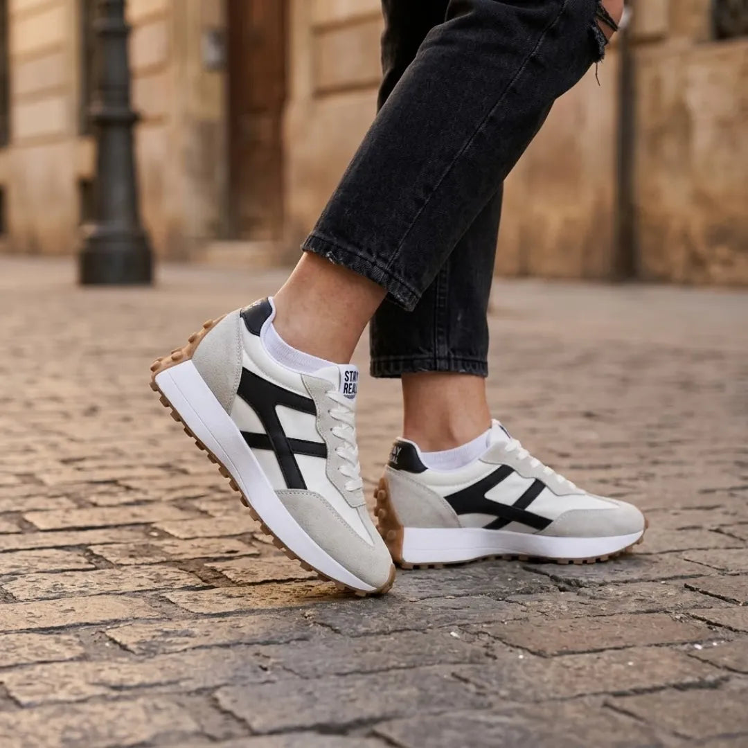 Sneakers gedragen door een model met zwarte jeans en witte sokken op een stenen straat 22
