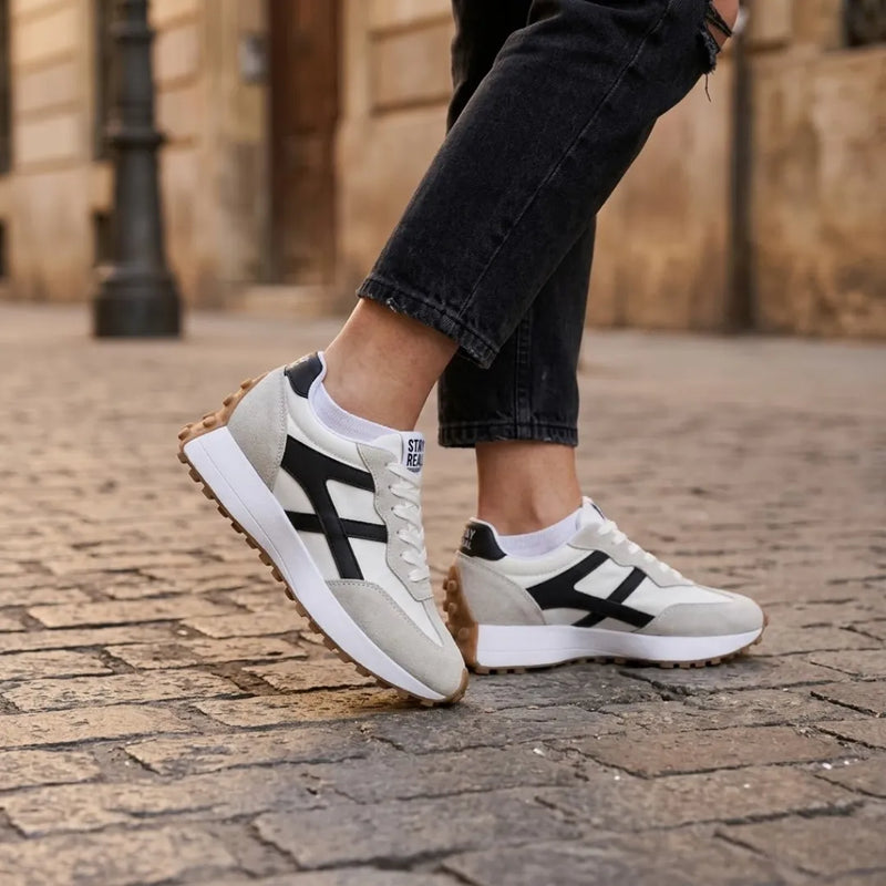 Sneakers gedragen door een model met zwarte jeans en witte sokken op een stenen straat 22