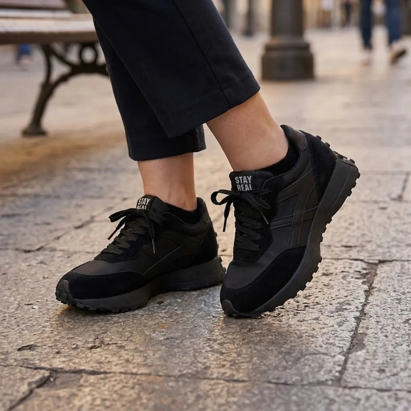 Zwarte sneakers gedragen met zwarte broek en sokken op een stenen straat 7