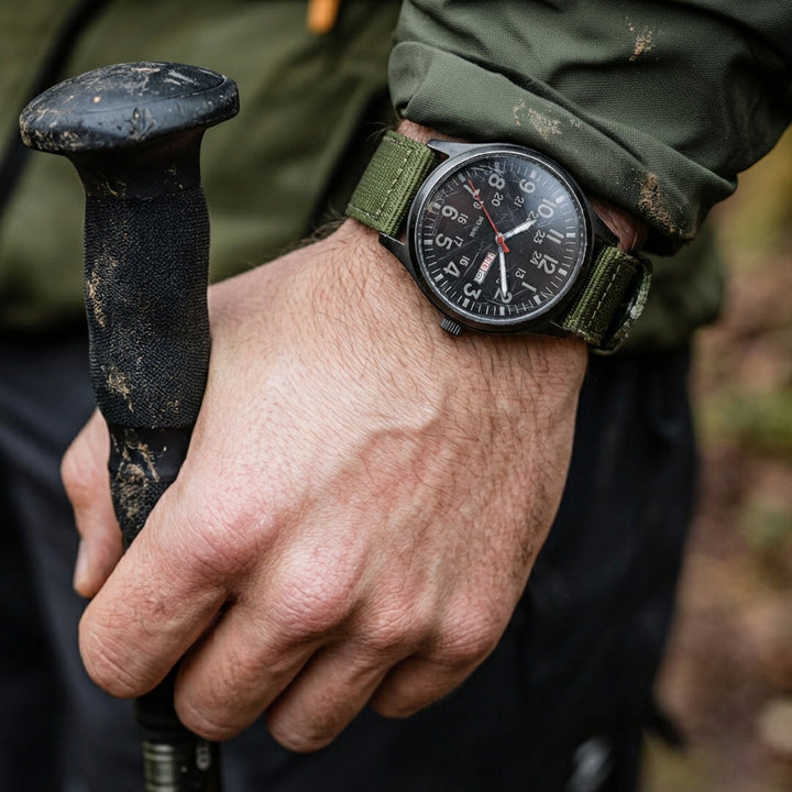 Het horloge om de pols van een wandelaar met modderige wandelstok, legergroene band en zwarte wijzerplaat in de natuur. 2