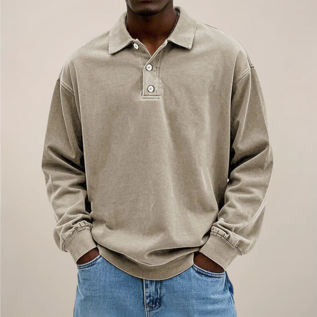 Model draagt de losse polo met lange mouwen en knoopsluiting in beige-grijs, gecombineerd met een lichtblauwe spijkerbroek. 6