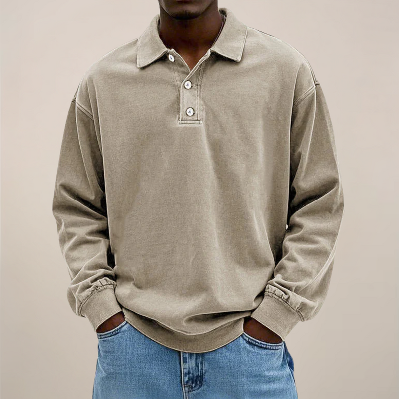 Model draagt de losse polo met lange mouwen en knoopsluiting in beige-grijs, gecombineerd met een lichtblauwe spijkerbroek. 6