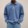 Model draagt de losse polo met lange mouwen en drie knopen in blauw, met handen in de zakken van een spijkerbroek. 1
