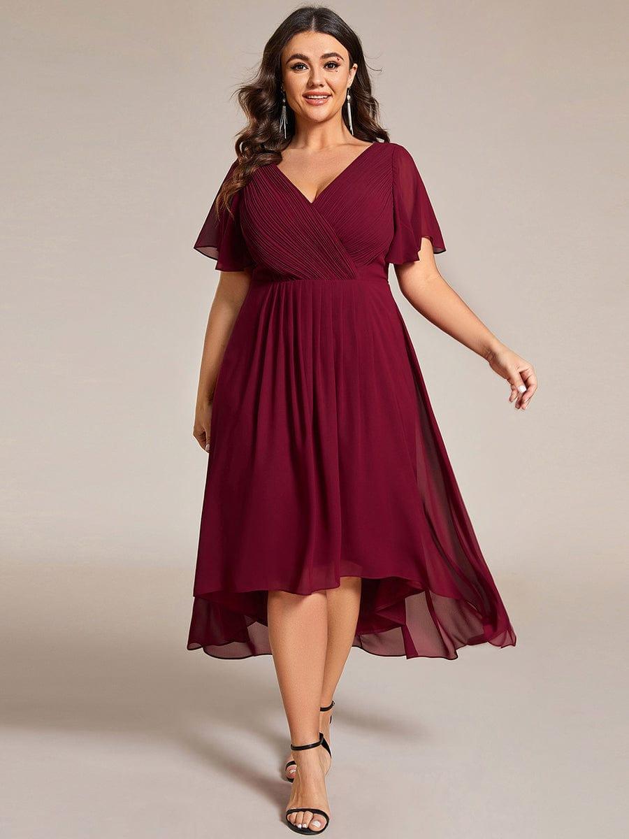 Model in grootte-ruime bordeauxrode chiffon jurk met V-hals en fladdermouwen, met lange oorbellen en zwarte sandalen. 49