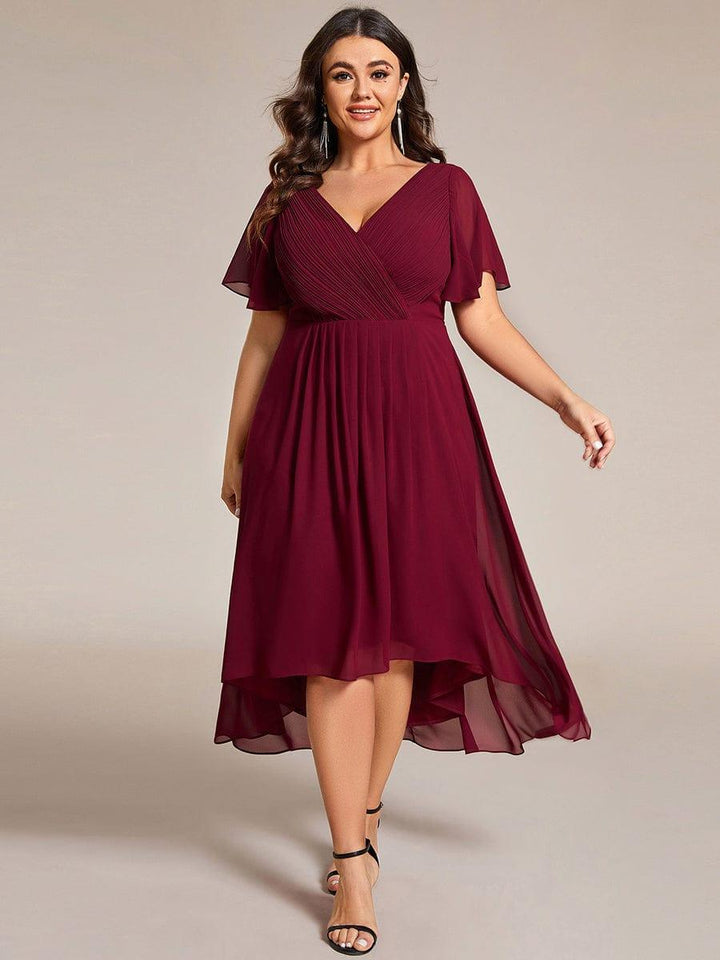 Model in grootte-ruime bordeauxrode chiffon jurk met V-hals en fladdermouwen, met lange oorbellen en zwarte sandalen. 49