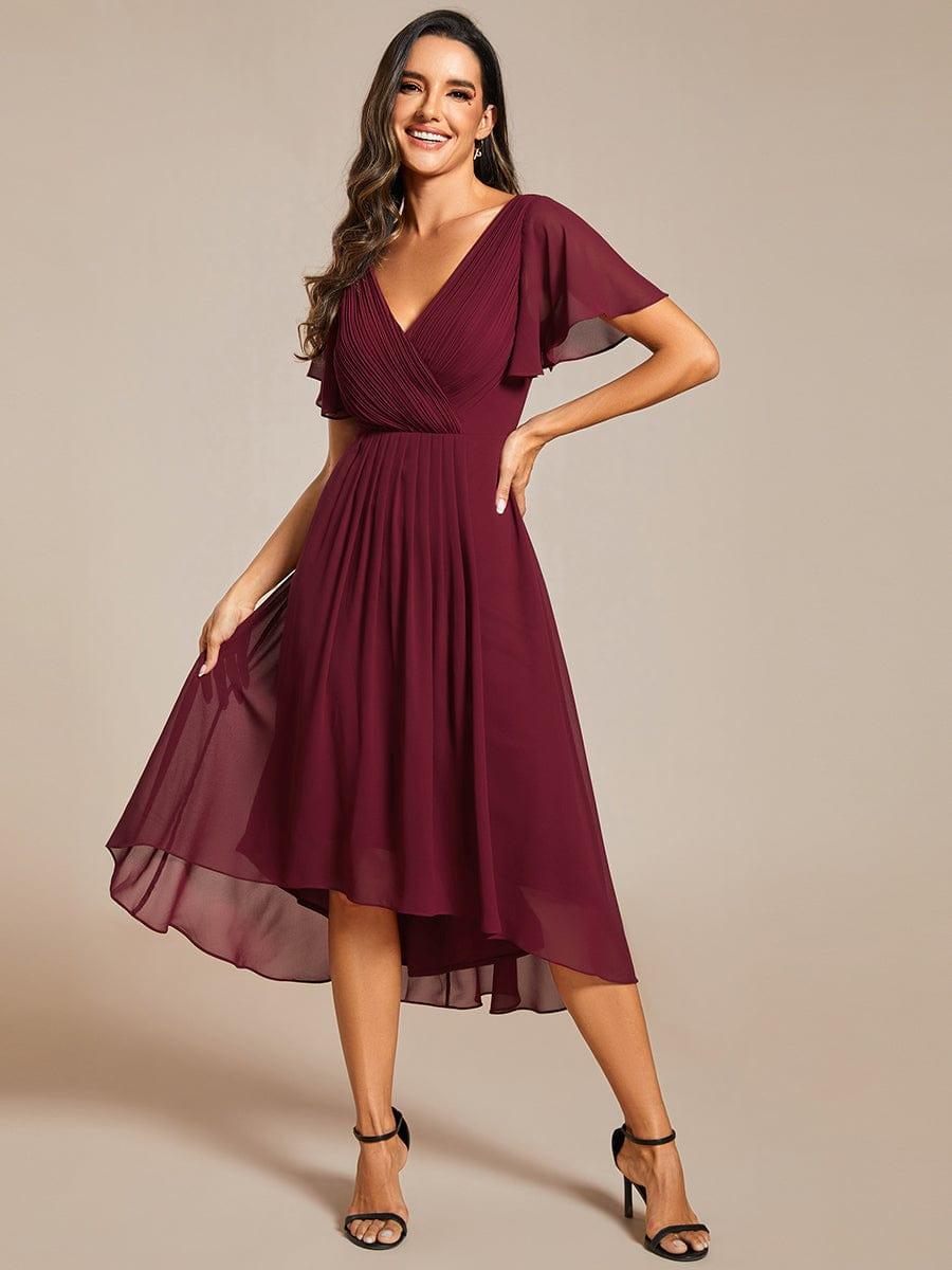 Bordeauxrode jurk van voren met hand op de heup, terwijl het model de wijde chiffon rok lichtjes optilt. 48