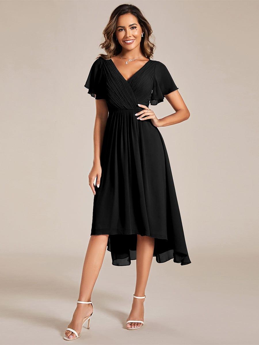 Zwarte jurk met V-hals en asymmetrische zoom, model poseert van voren met een hand op de heup. 21