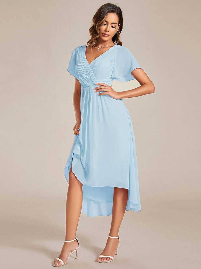 Lichtblauwe jurk in driekwartaanzicht, model tilt de wapperende chiffon rok lichtjes op met een hand op de heup. 88