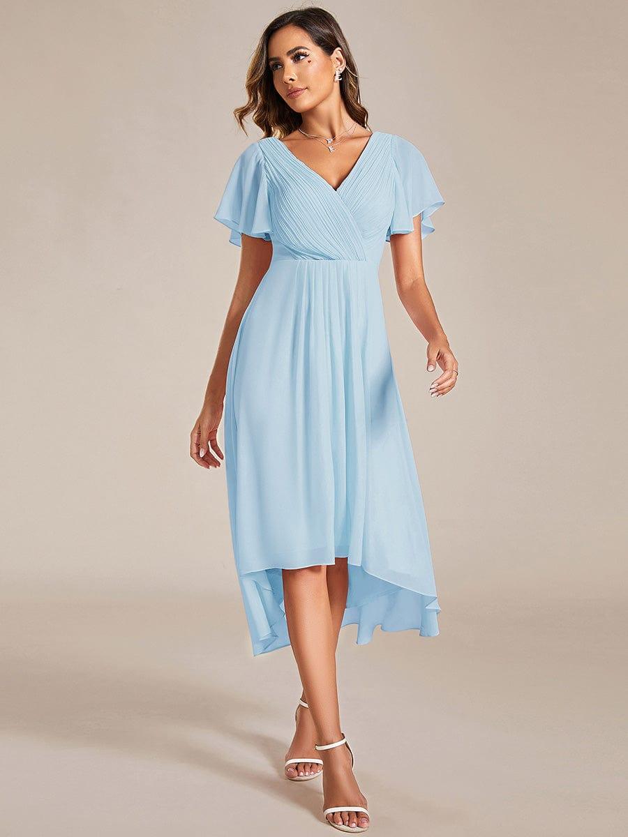 Model in lichtblauwe chiffon jurk met gekruiste V-hals en korte fladdermouwen, loopt naar voren in witte sandalen. 84