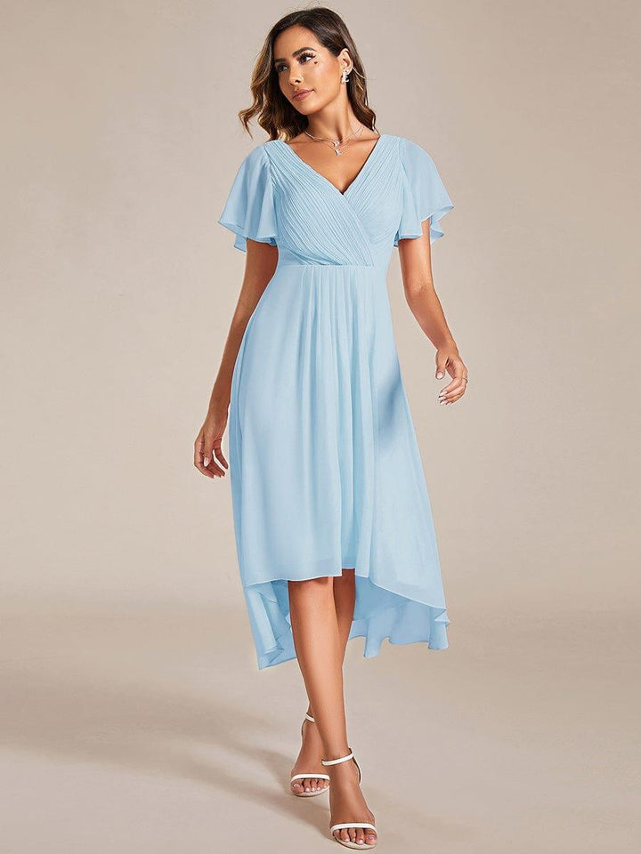 Model in lichtblauwe chiffon jurk met gekruiste V-hals en korte fladdermouwen, loopt naar voren in witte sandalen. 84