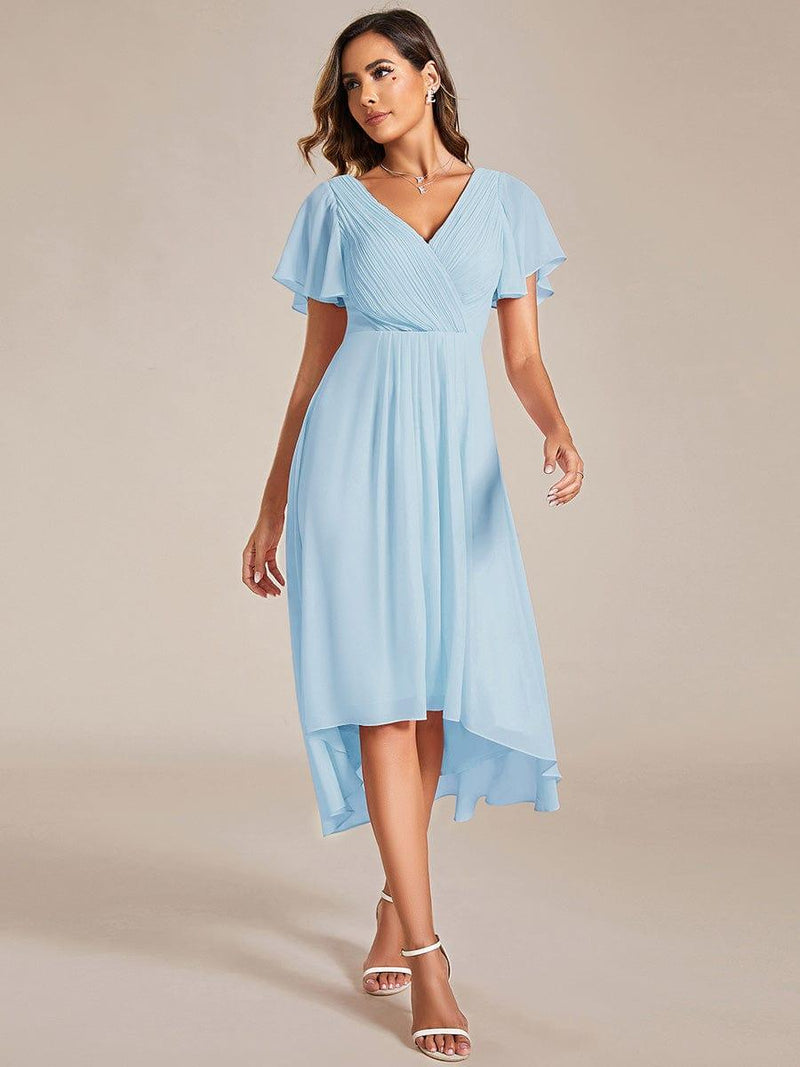 Model in lichtblauwe chiffon jurk met gekruiste V-hals en korte fladdermouwen, loopt naar voren in witte sandalen. 84