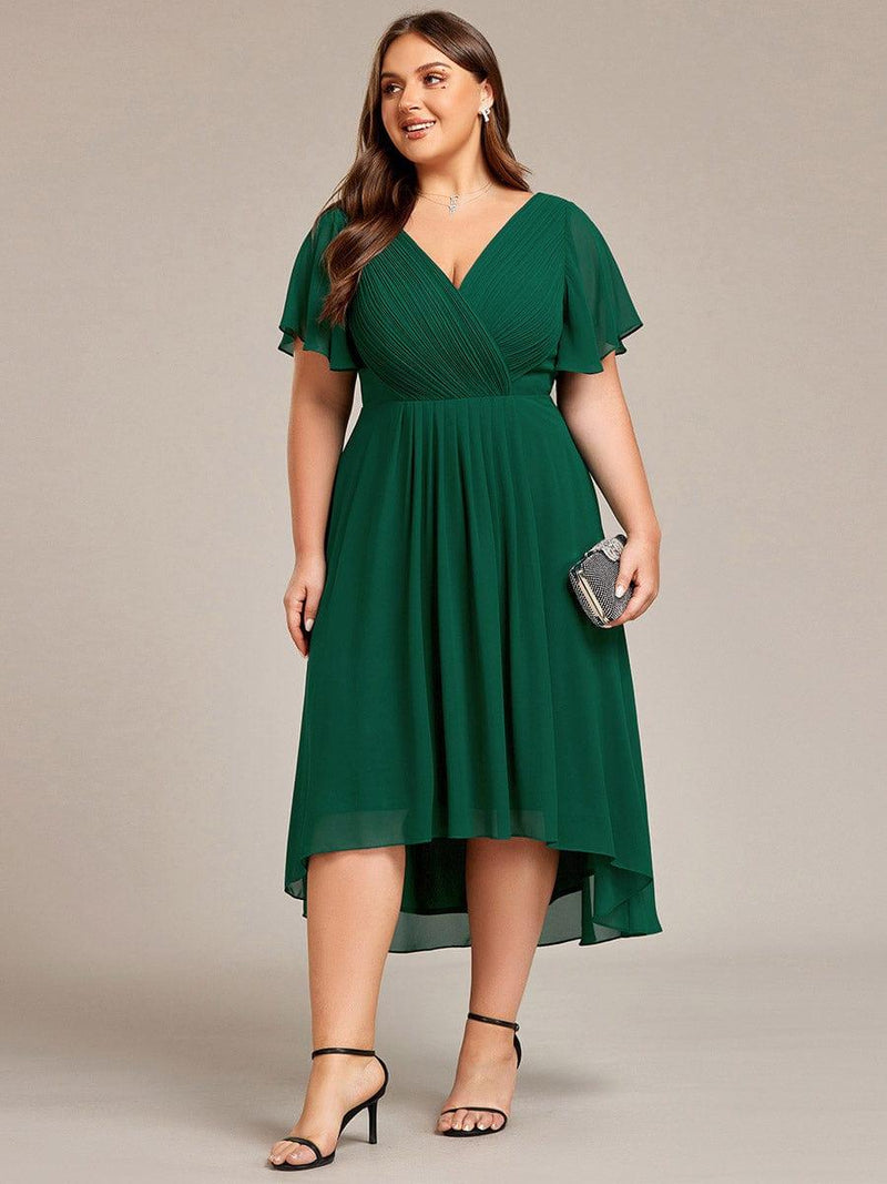 Donkergroene jurk in grotere maat van voren, model draagt een glinsterende clutch en zwarte sandalen. 40