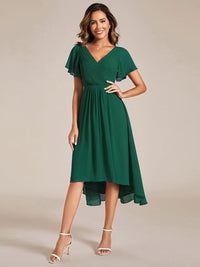 Donkergroene jurk met gedrapeerd lijfje, vlindermouwen en asymmetrische zoom, model met hand op de heup, voorkant 10
