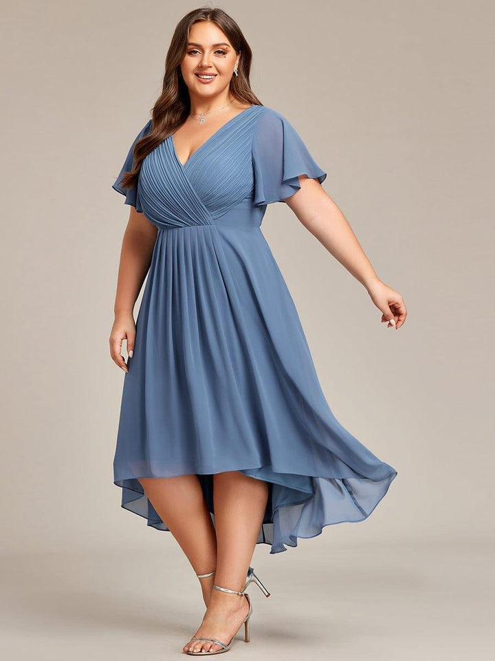 Model draait in de dusty blauwe jurk zodat de lichte, asymmetrische chiffon rok wappert. 45