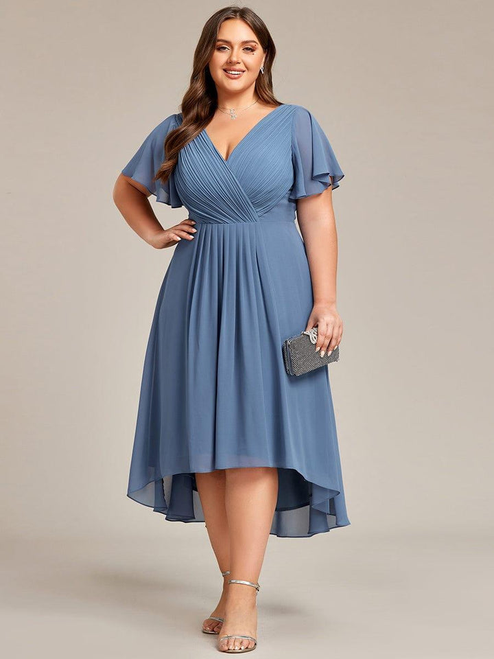 Dusty blauwe chiffon jurk met hand op de heup en glinsterend clutchtasje, van voren gezien op een model. 44