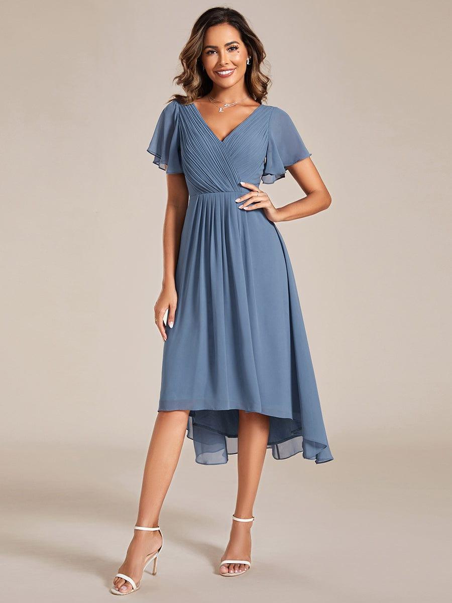 Stofblauwe jurk met gedrapeerd lijfje en wijd uitlopende zoom, model met hand op de heup en witte sandalen, voorkant 5