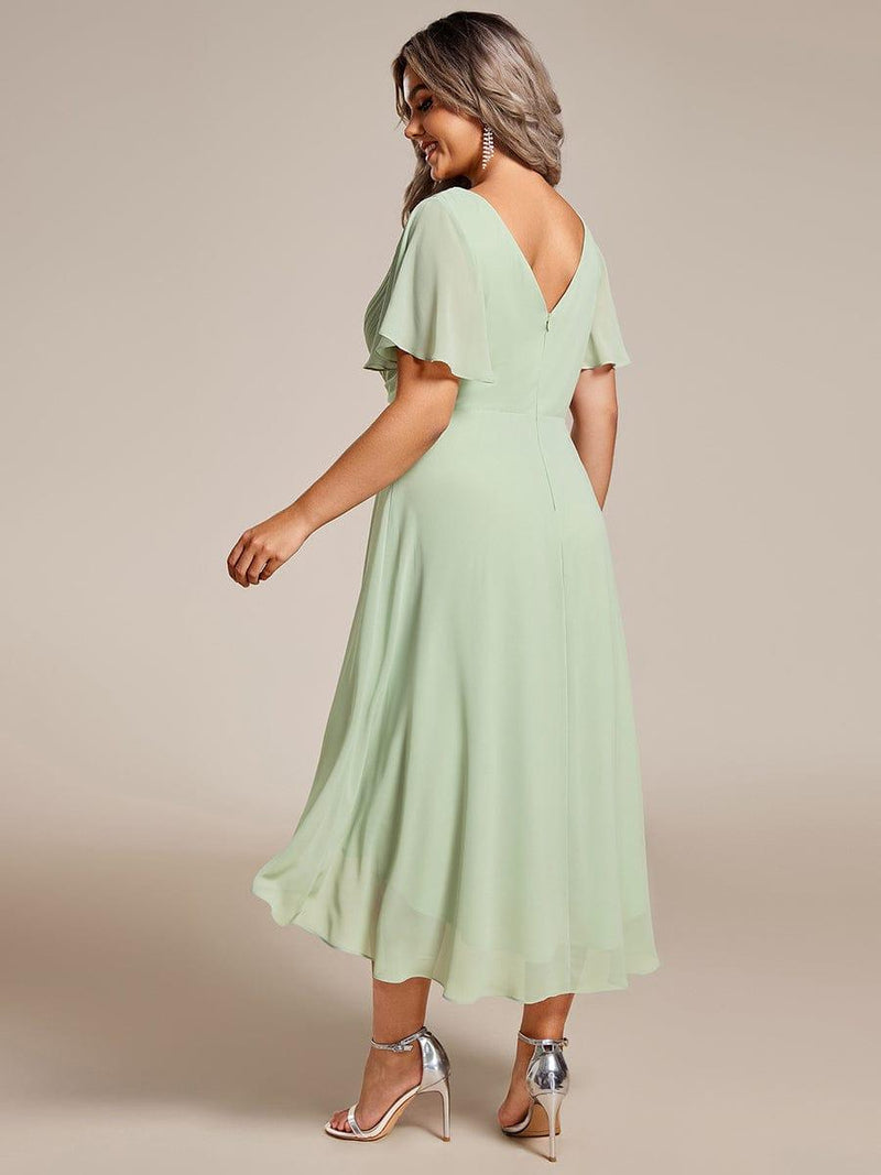 Achterkant van de saliegroene jurk met diepe V-rug, rits en wijd uitlopende asymmetrische chiffon rok. 82