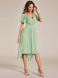 Model in saliegroene jurk met asymmetrische zoom, hand bij het hoofd, schuin van voren gefotografeerd. 80