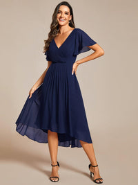 Marineblauwe jurk van voren, model houdt de wijde asymmetrische chiffon rok met één hand vast. 54
