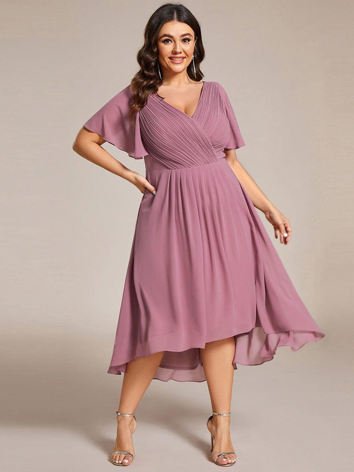 Model met maatje meer in oudroze jurk, hand op de heup, met gouden sandalen en lange oorbellen. 66