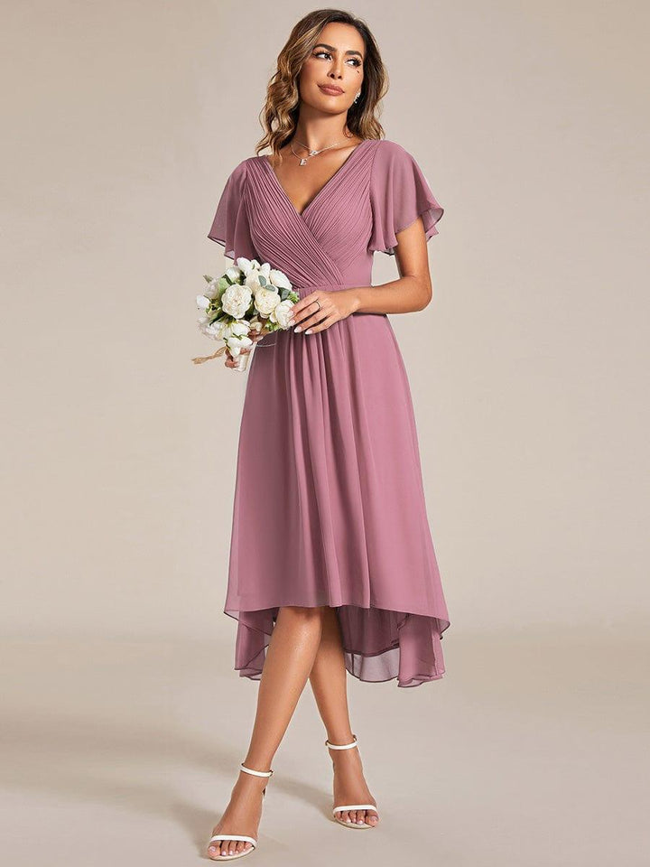 Model in oudroze chiffon jurk houdt een boeket witte bloemen vast, gekleed met witte sandalen. 60