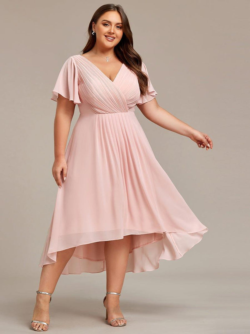 Roze jurk in grotere maat van voren, model glimlacht en laat de asymmetrische zoom zwieren. 34