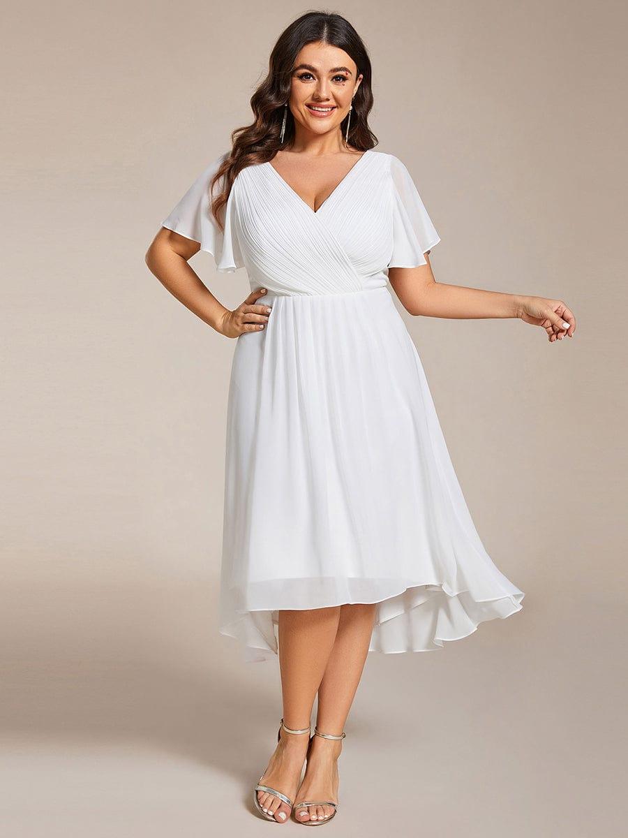 Model met maatje meer in witte jurk met V-hals, hand op de heup en gouden sandalen. 73