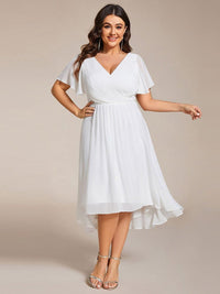 Model met maatje meer in witte jurk met V-hals, hand op de heup en gouden sandalen. 73