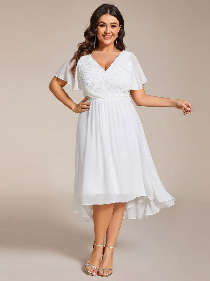 Model met maatje meer in witte jurk met V-hals, hand op de heup en gouden sandalen. 73