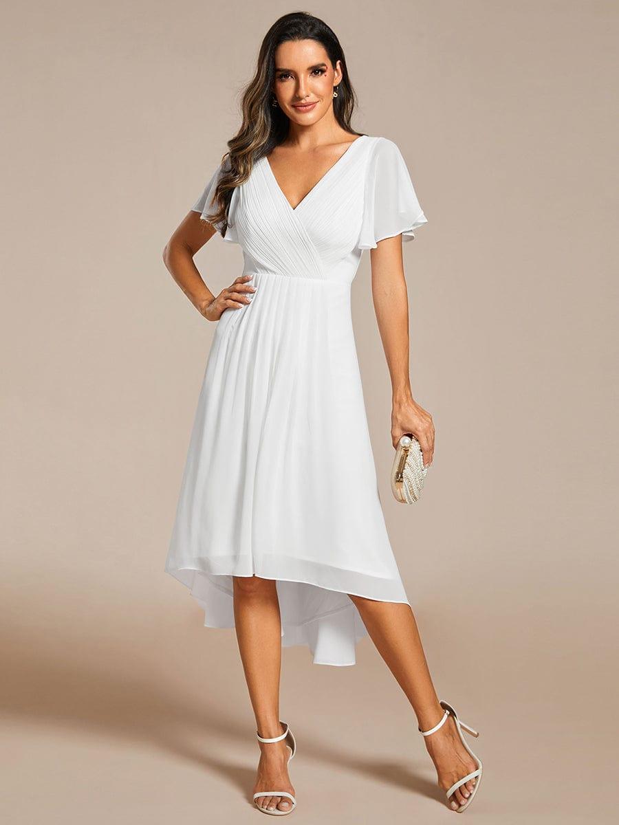 Model in witte jurk, hand op de heup, met parelclutch en sandalen met enkelbandje. 71