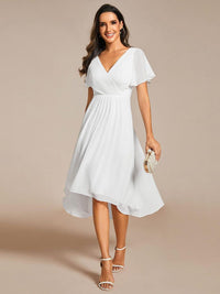 Model in witte jurk met V-hals en asymmetrische zoom, met parelclutch in de hand en witte sandalen. 68
