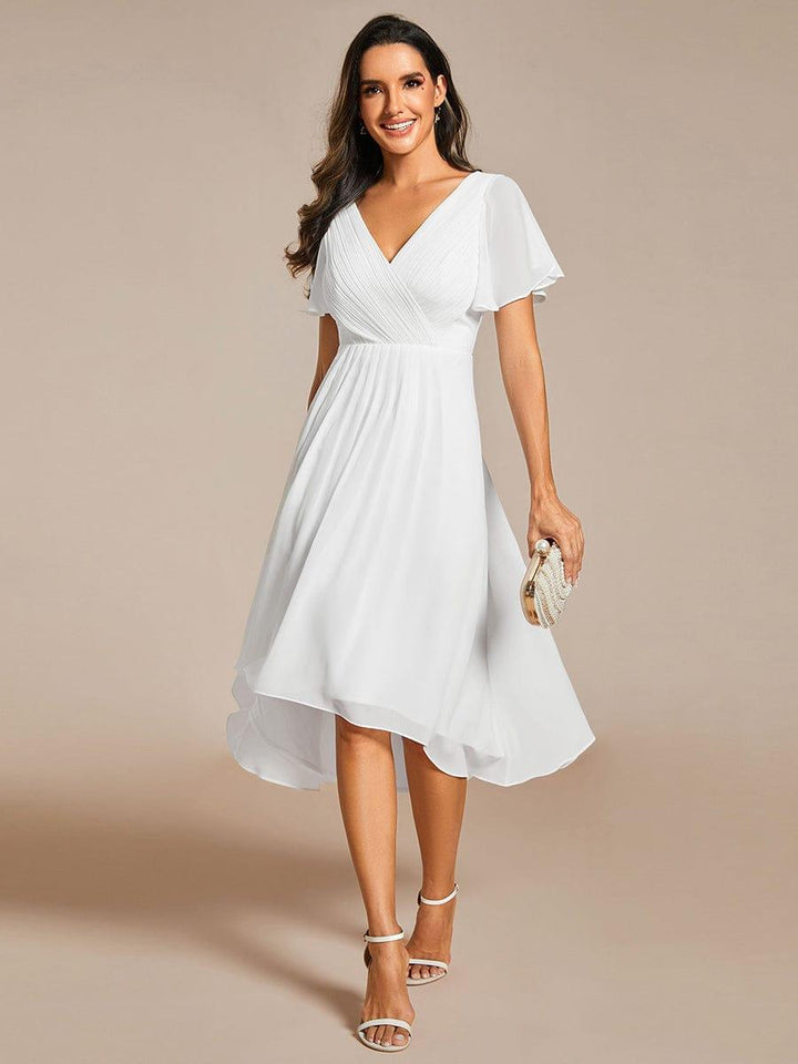 Model in witte jurk met V-hals en asymmetrische zoom, met parelclutch in de hand en witte sandalen. 68