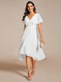 Model in witte jurk met V-hals en asymmetrische zoom, met parelclutch in de hand en witte sandalen. 68