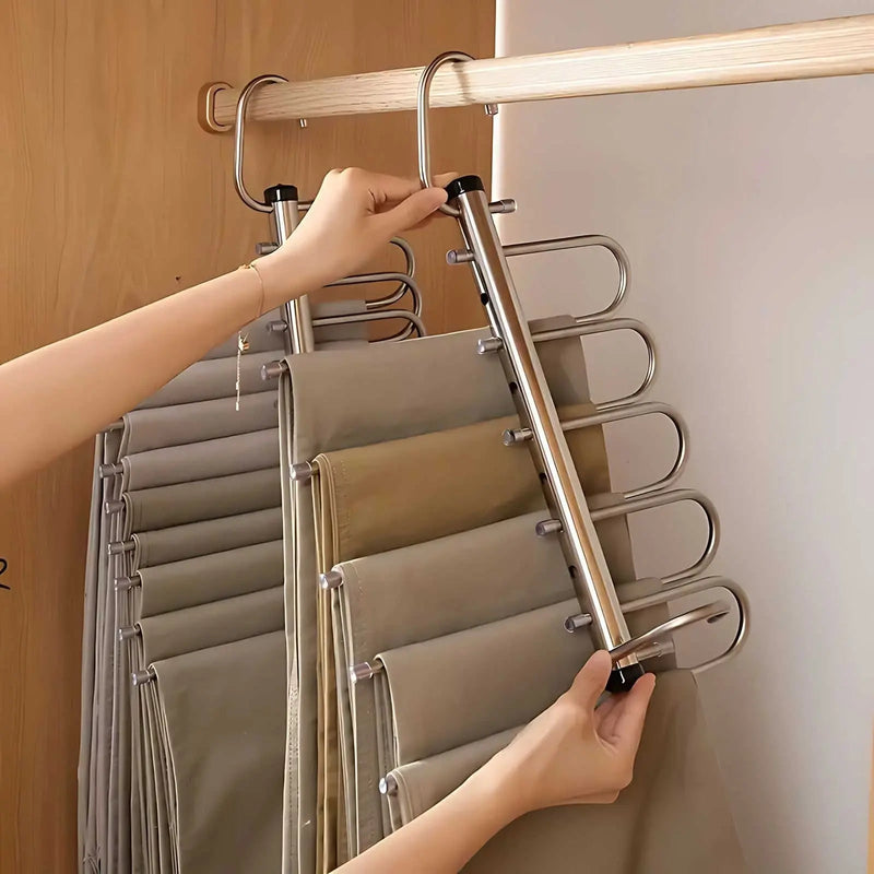Twee handen houden het uitgeklapte rek vast, met naast elkaar hangende broeken en daarachter een tweede rek. 3