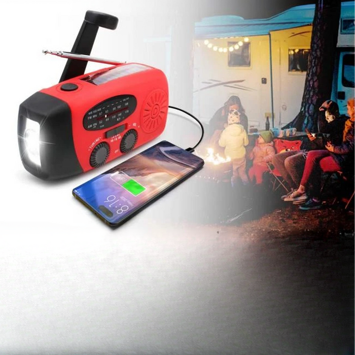 Rode noodradio laadt een telefoon op, met op de achtergrond mensen bij een kampvuur voor een camper 4