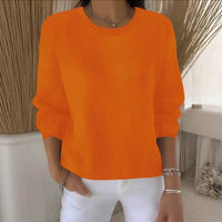 Oranje gebreide trui met ronde hals, gedragen door een model in een lichte kamer met witte broek 11