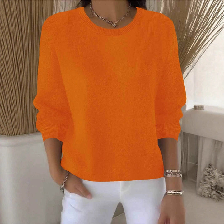 Oranje gebreide trui met ronde hals, gedragen door een model in een lichte kamer met witte broek 11