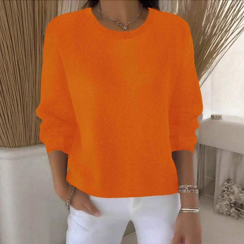 Oranje gebreide trui met ronde hals, gedragen door een model in een lichte kamer met witte broek 11