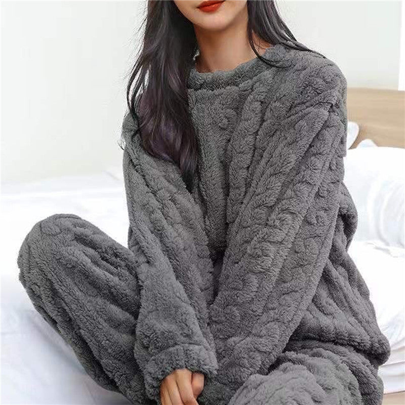 Vrouw in grijze fleece pyjamaset met reliëfpatroon, zittend op een bed met wit beddengoed 4